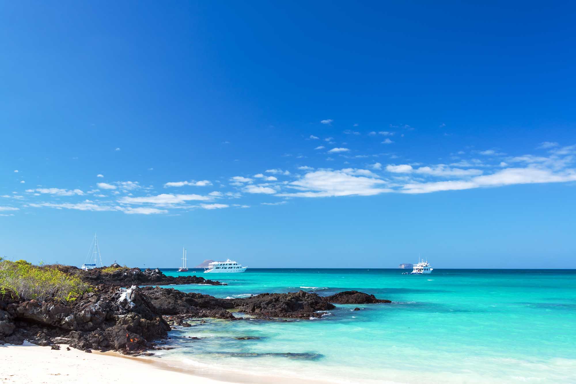 A stunning tropical beach scene featuring crystal-clear turquoise waters, dark volcanic rock