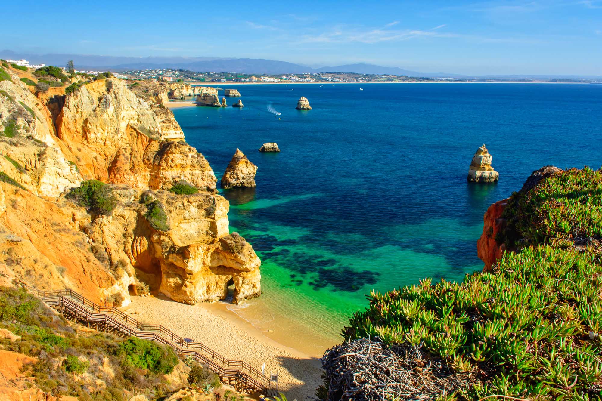 A stunning coastal view of Praia do Camilo beach featuring golden sandstone cliffs, crystal-clear