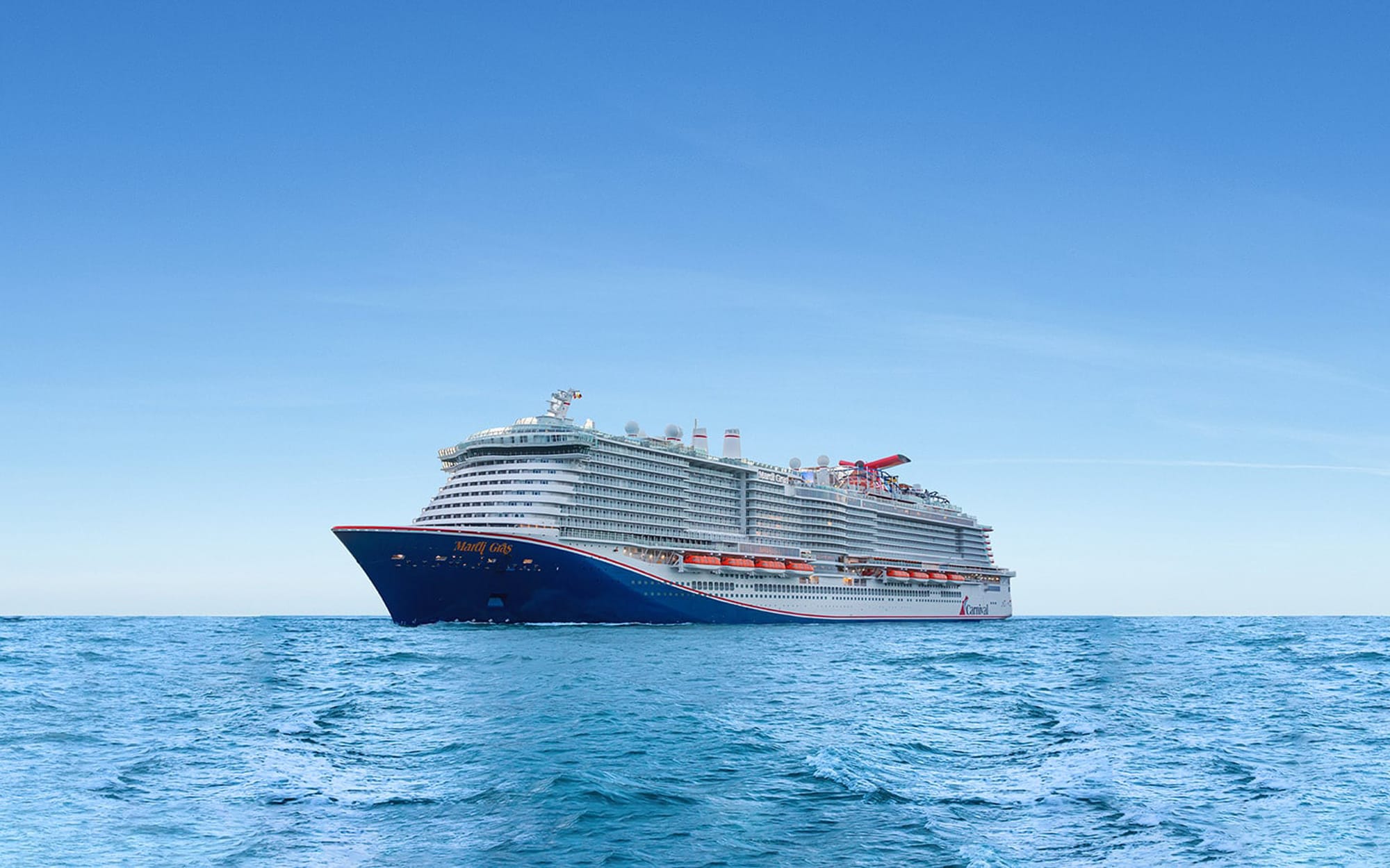 A large, modern Carnival cruise ship sailing on calm, blue waters under a clear sky. The vessel