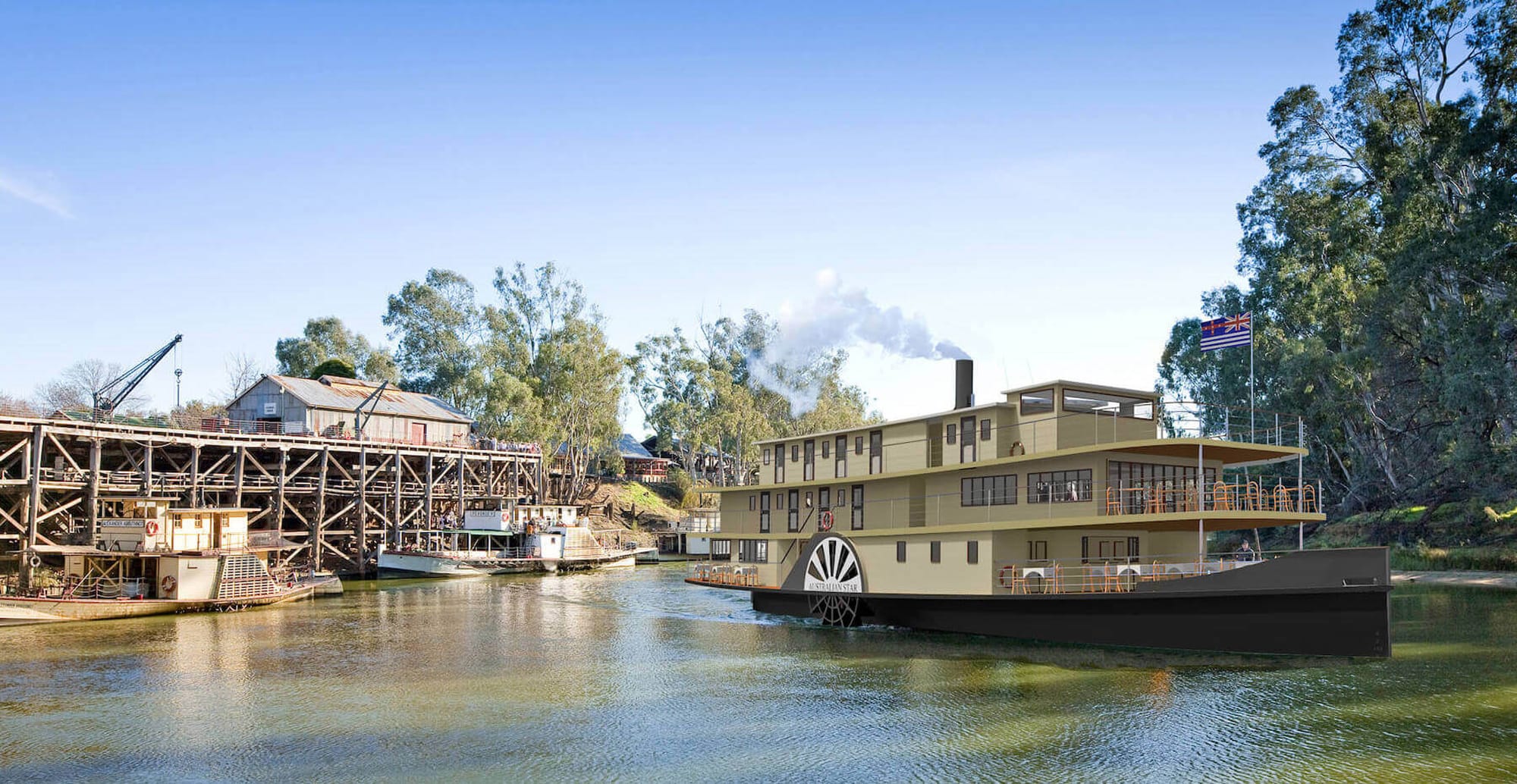 A historic paddlewheel riverboat moored along a scenic river with trees and industrial structures