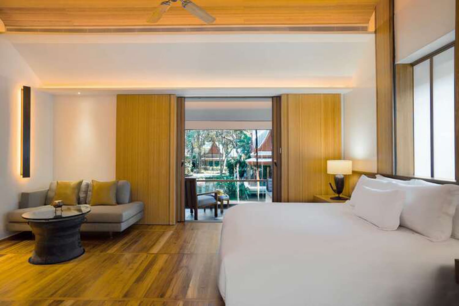 Luxury hotel suite with king bed, lounge area, and balcony overlooking tropical gardens