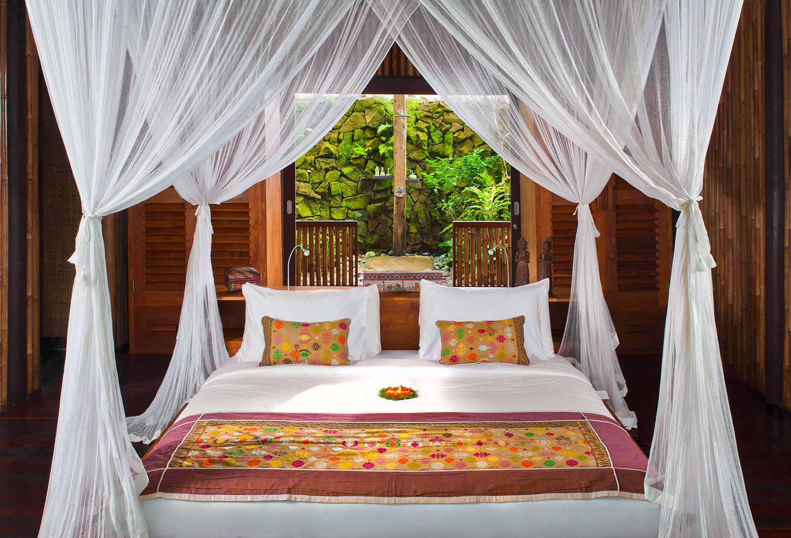 Four-poster bed with white sheer canopy curtains in tropical villa bedroom with garden view