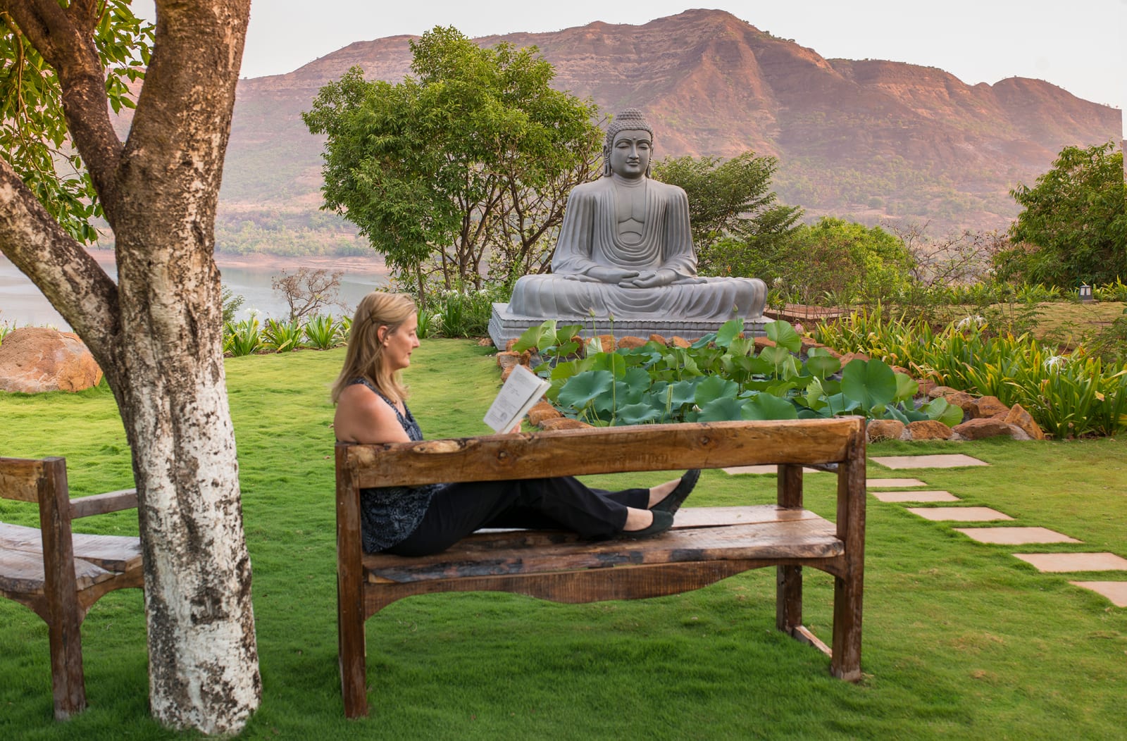 Woman relaxing on wooden bench with Buddha statue and mountain lake in background