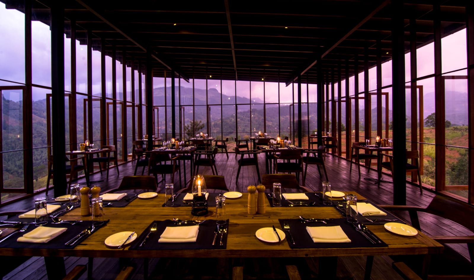 Modern dining room with floor-to-ceiling windows overlooking purple-lit mountains at dusk