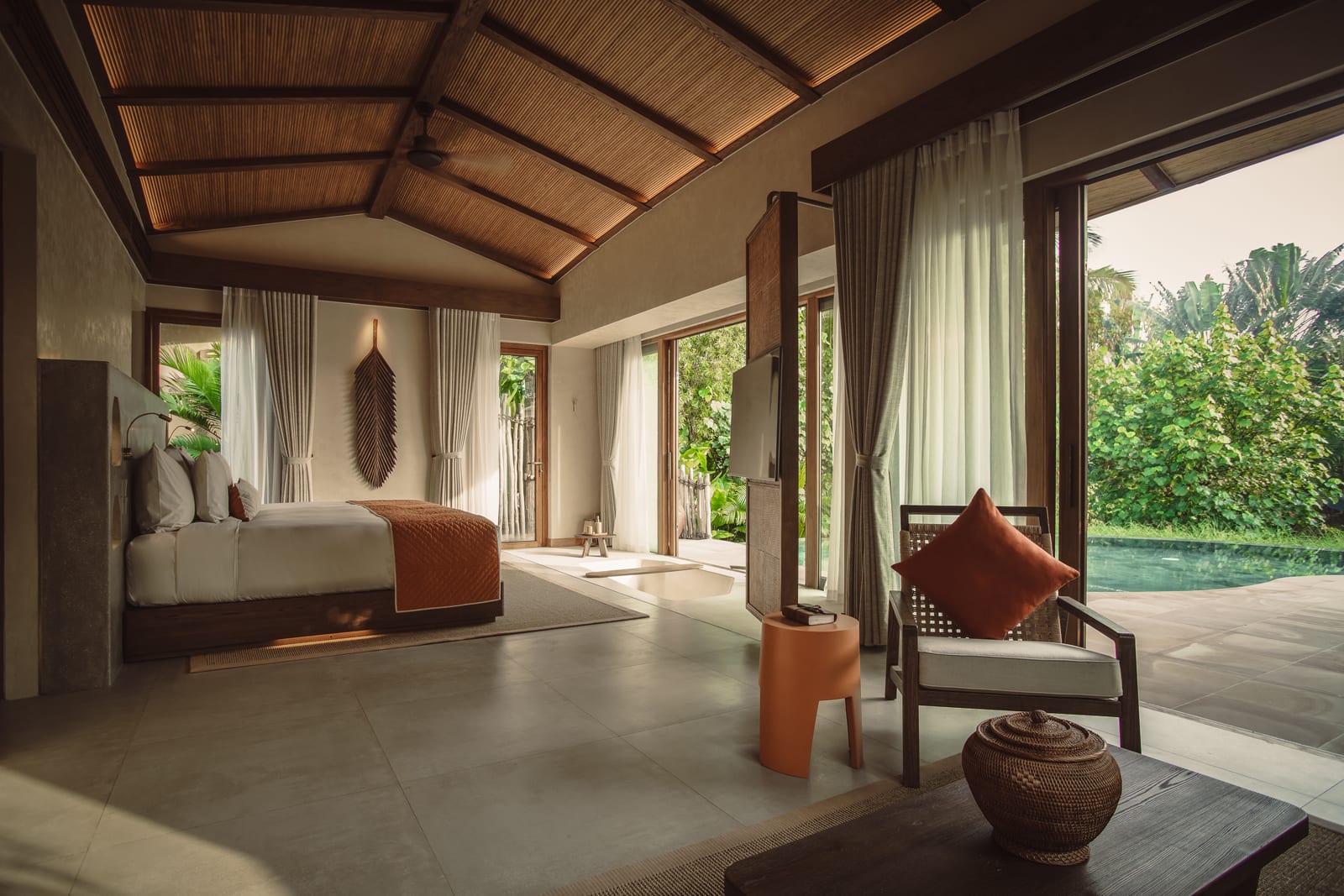 Luxury resort bedroom with wooden ceiling, pool view, and tropical gardens visible through open doors