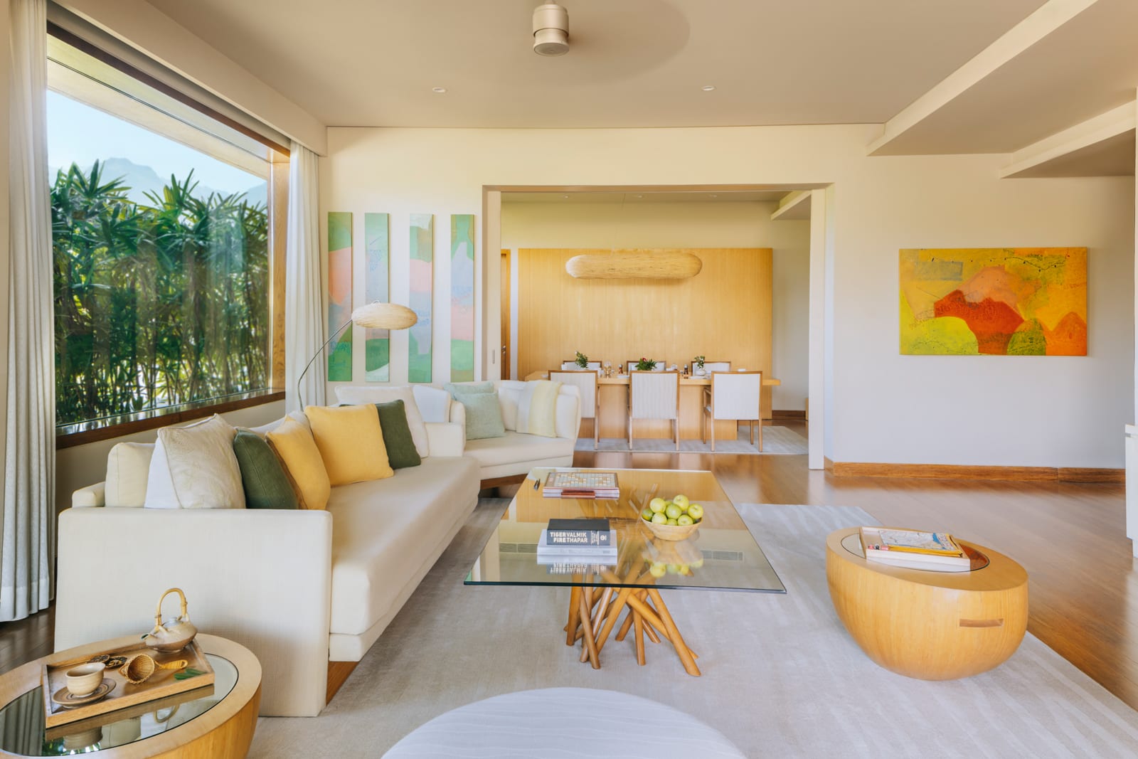 Modern luxury suite living room with cream sectional sofa, wooden coffee table, and tropical garden view through floor-to-ceiling windows