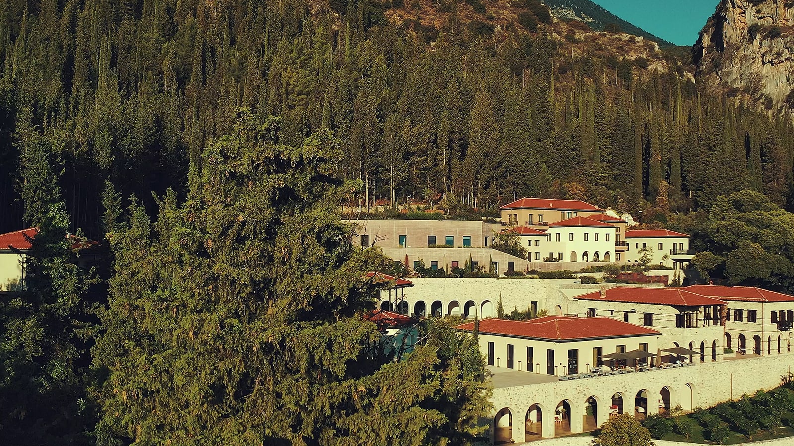 Mountain resort with cream buildings and red-tile roofs nestled among tall evergreen forest