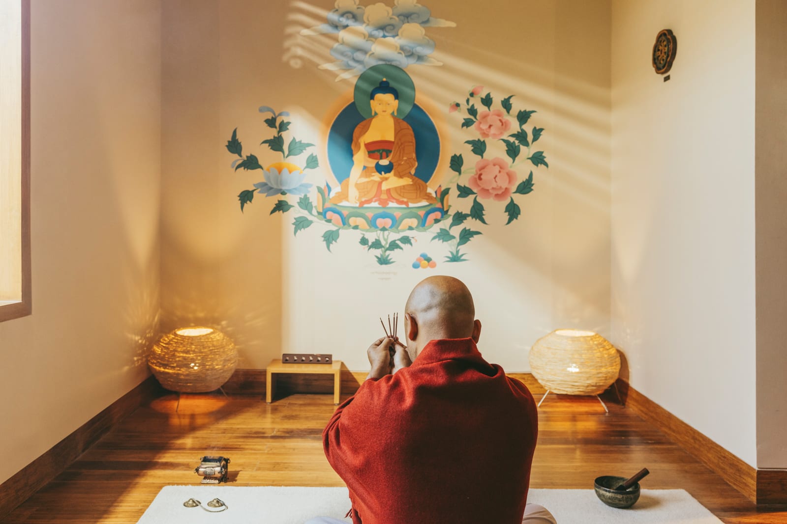 Buddhist monk meditating in shrine room with deity artwork and incense