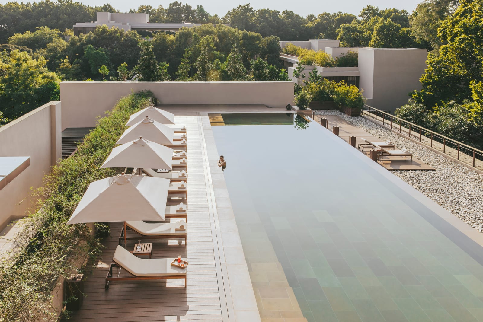 Modern resort with rectangular pool, sun loungers, and umbrellas surrounded by forested landscape