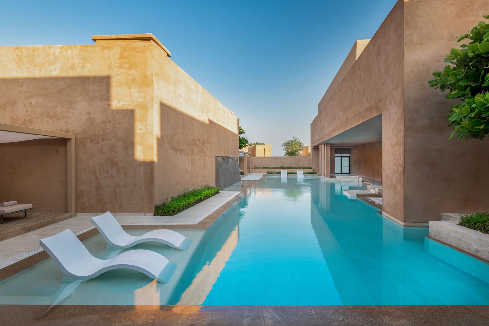 Modern spa courtyard with turquoise lap pool, white loungers, and earth-toned architecture