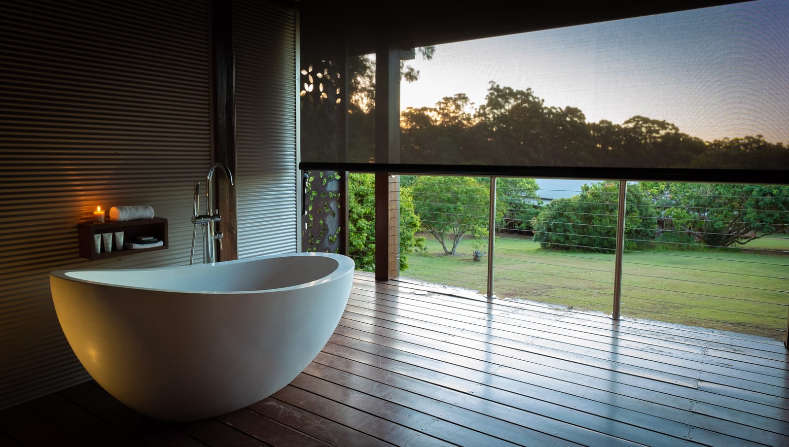 Modern white freestanding bathtub on wooden deck overlooking green lawn and trees