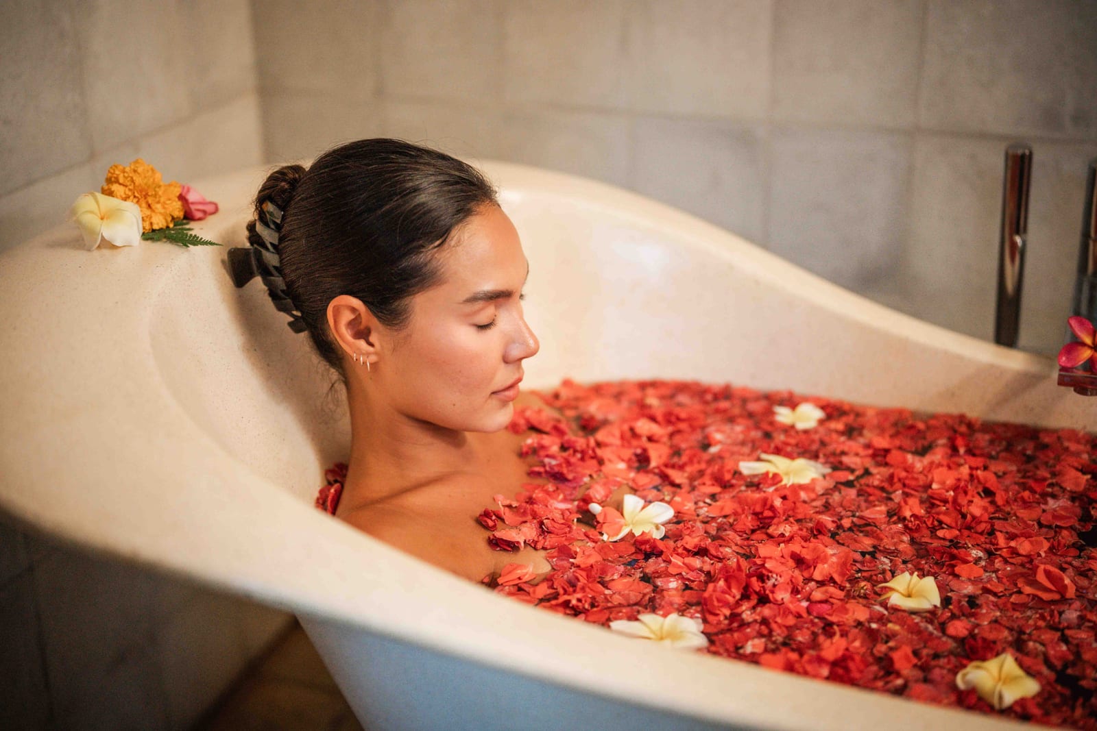 Woman in bathtub with braided updo, soaking in water filled with red flower petals