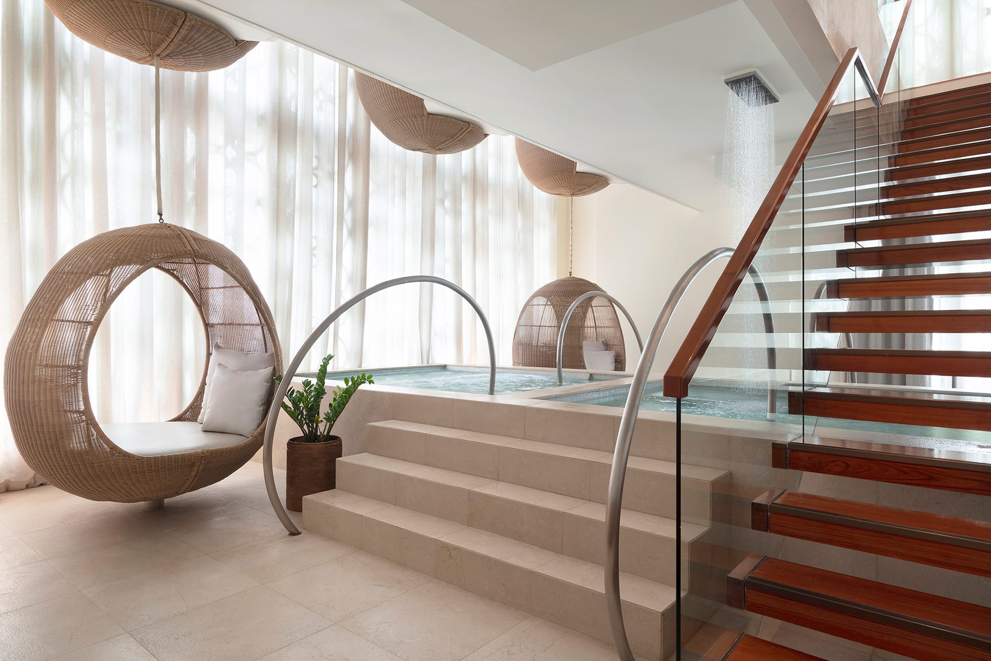 Modern spa interior with woven hanging chairs, indoor pool, and wooden staircase with glass railing