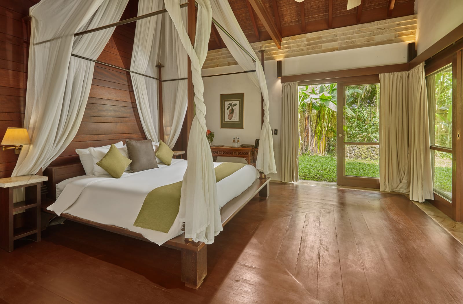 Luxury bedroom with wooden canopy bed, sheer white curtains, and floor-to-ceiling windows overlooking tropical garden