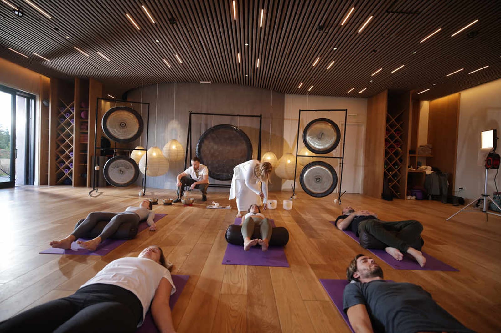 Yoga class in modern studio with gong wall installation and instructor leading relaxation pose