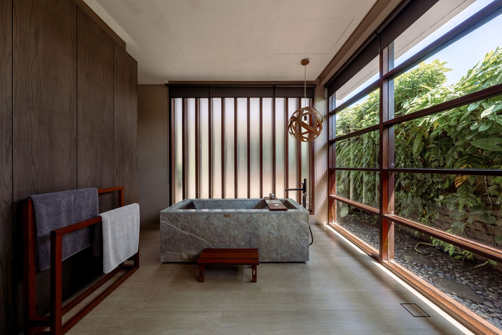 Modern spa bathroom with stone soaking tub, wooden railings, and garden views through large windows