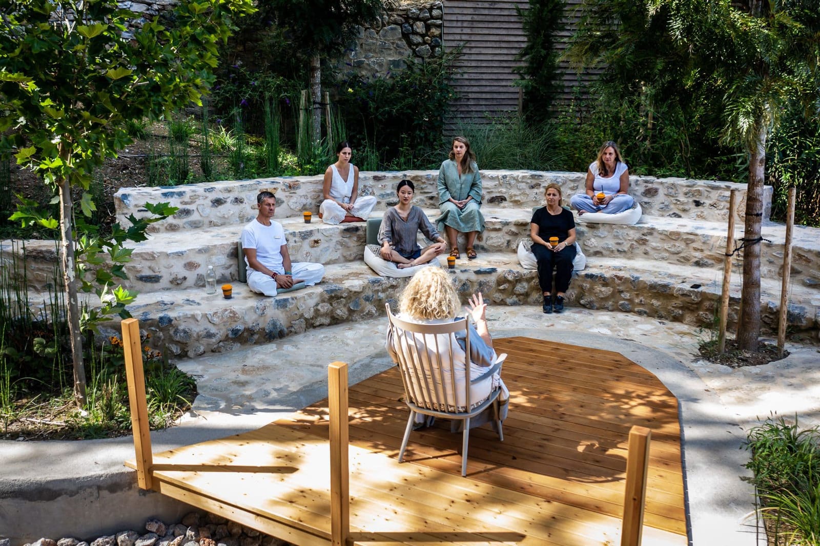 Group gathered in stone amphitheater for outdoor wellness session with wooden platform stage