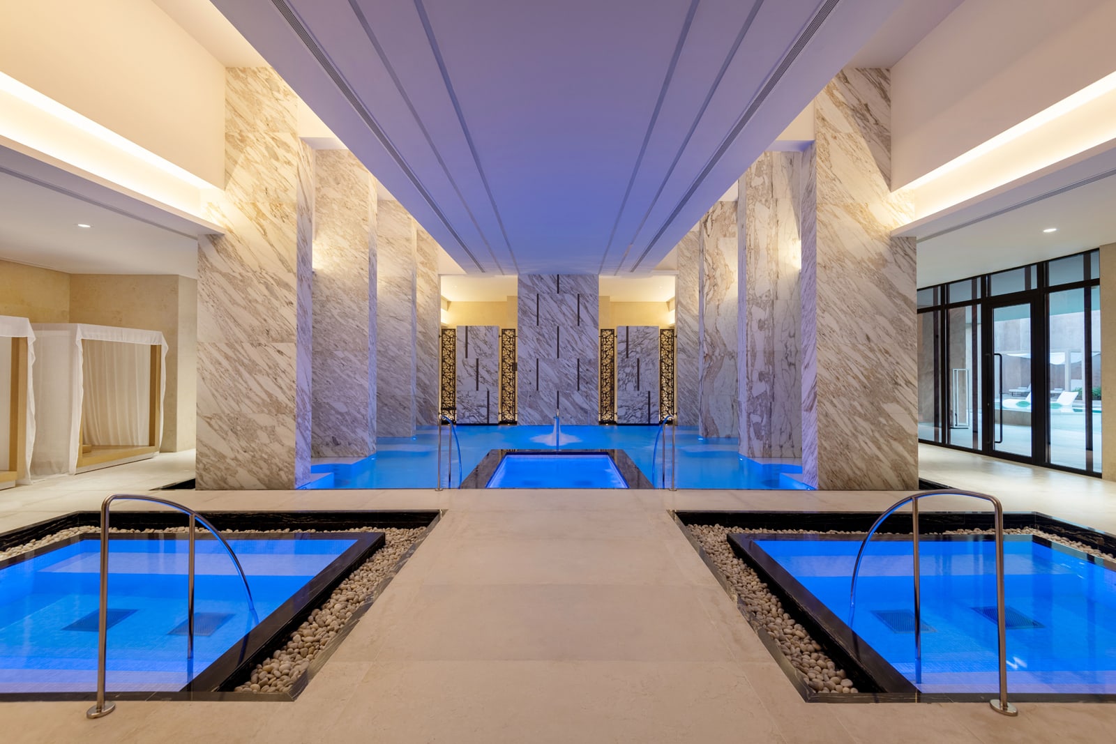 Luxury spa hydrothermal pool with bright blue water, marble columns, and modern ceiling lighting