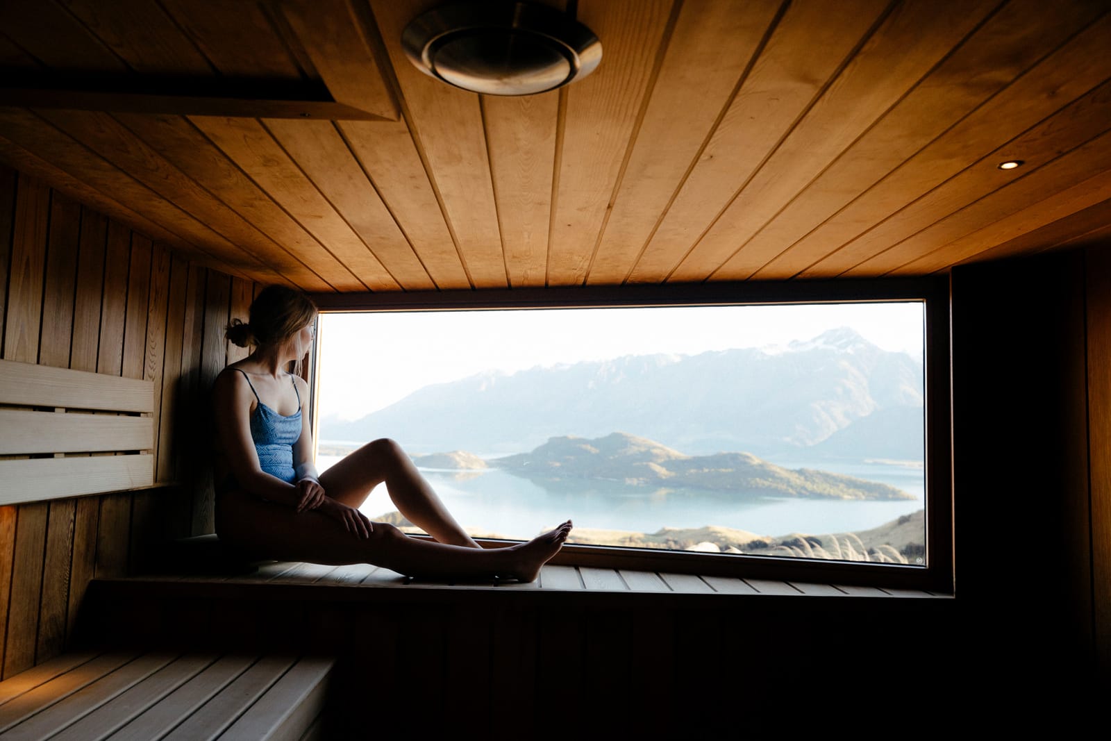 Woman relaxing in wooden sauna with mountain lake view through window