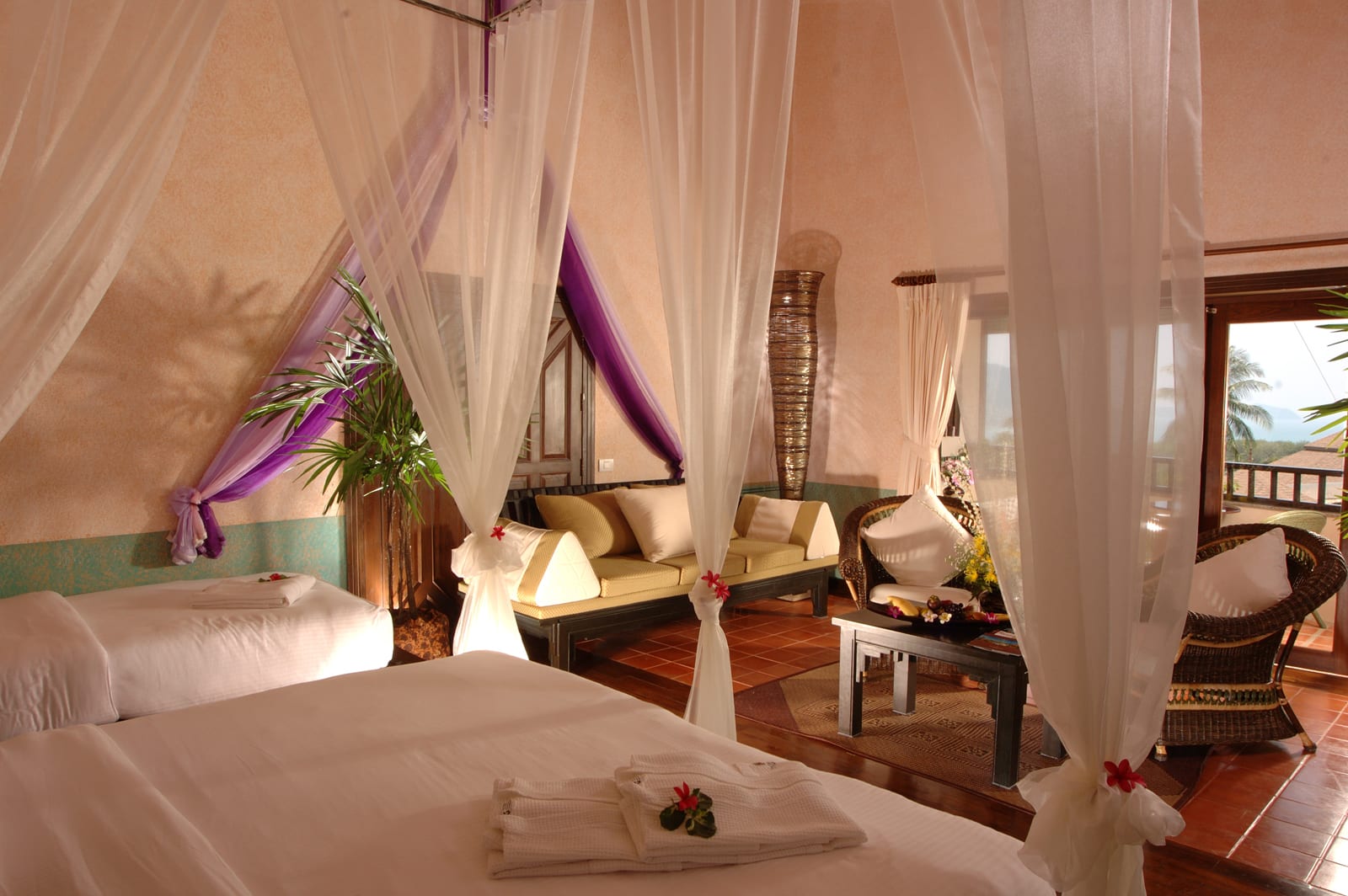 Luxury resort bedroom with sheer white canopy drapes, lounging area, and ocean-view balcony