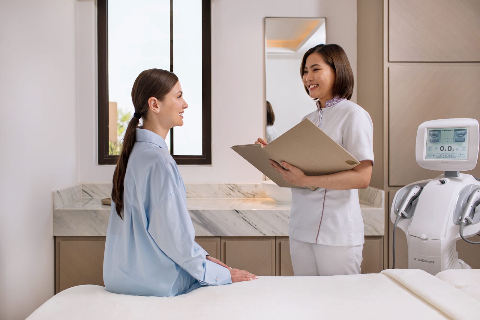 Healthcare provider in white uniform holding clipboard consulting with patient in medical spa treatment room