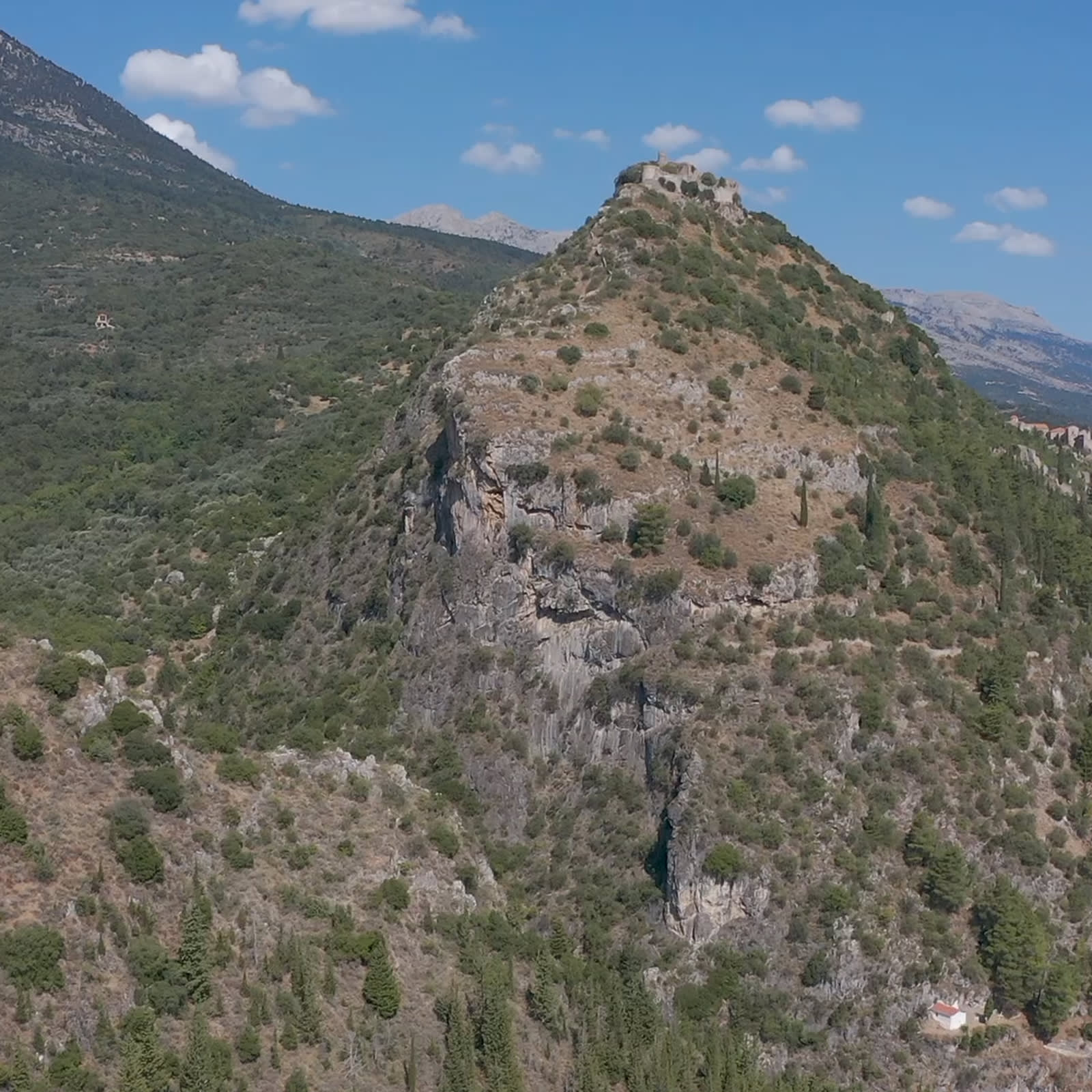 Rocky hilltop fortress with ruins overlooking forested mountain valley under blue sky