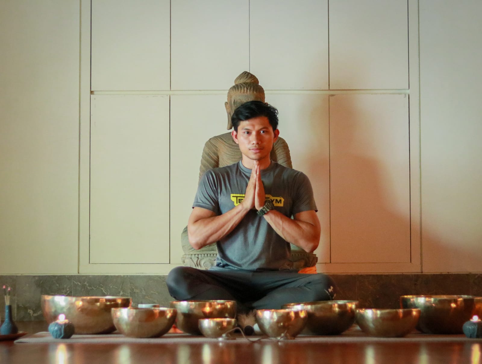 Man in meditation pose with hands pressed together, sitting in front of lit singing bowls