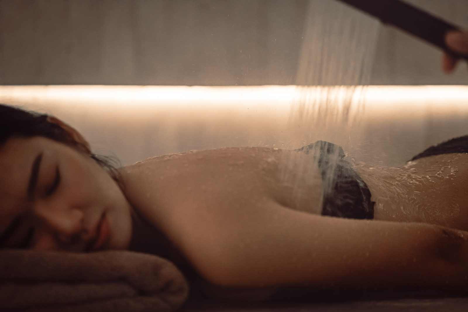 Person relaxing in steaming hammam bath with warm water and steam rising