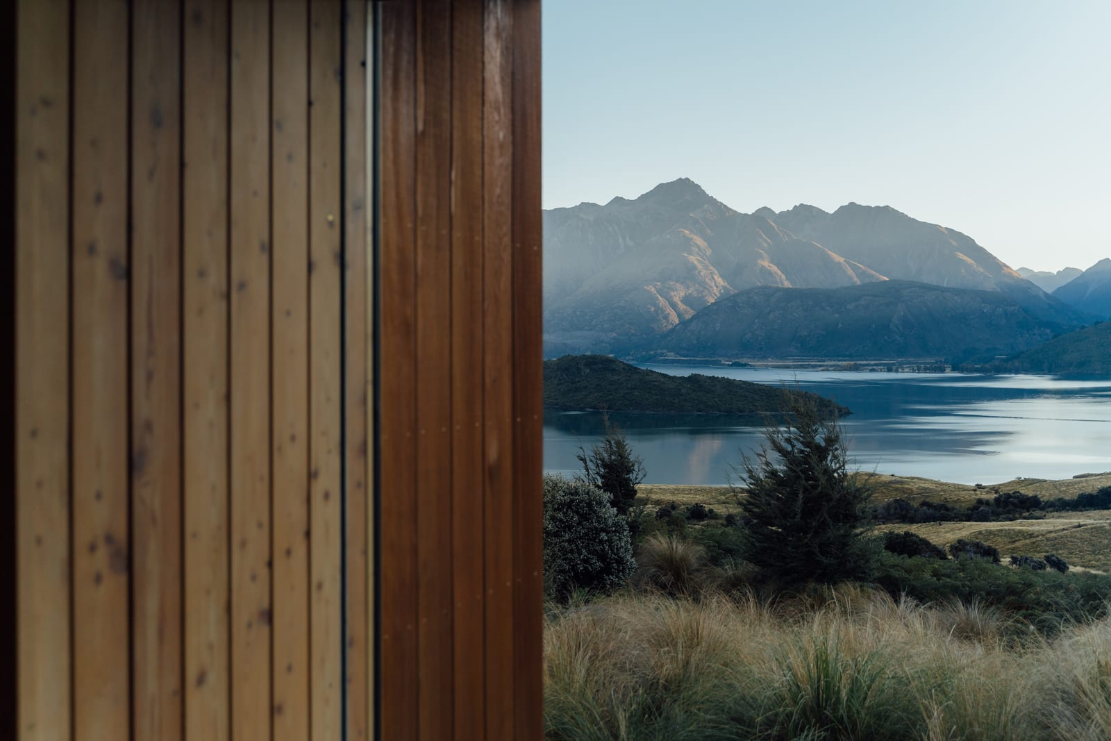 Wooden deck railing with view of mountains, lake, and native grasses