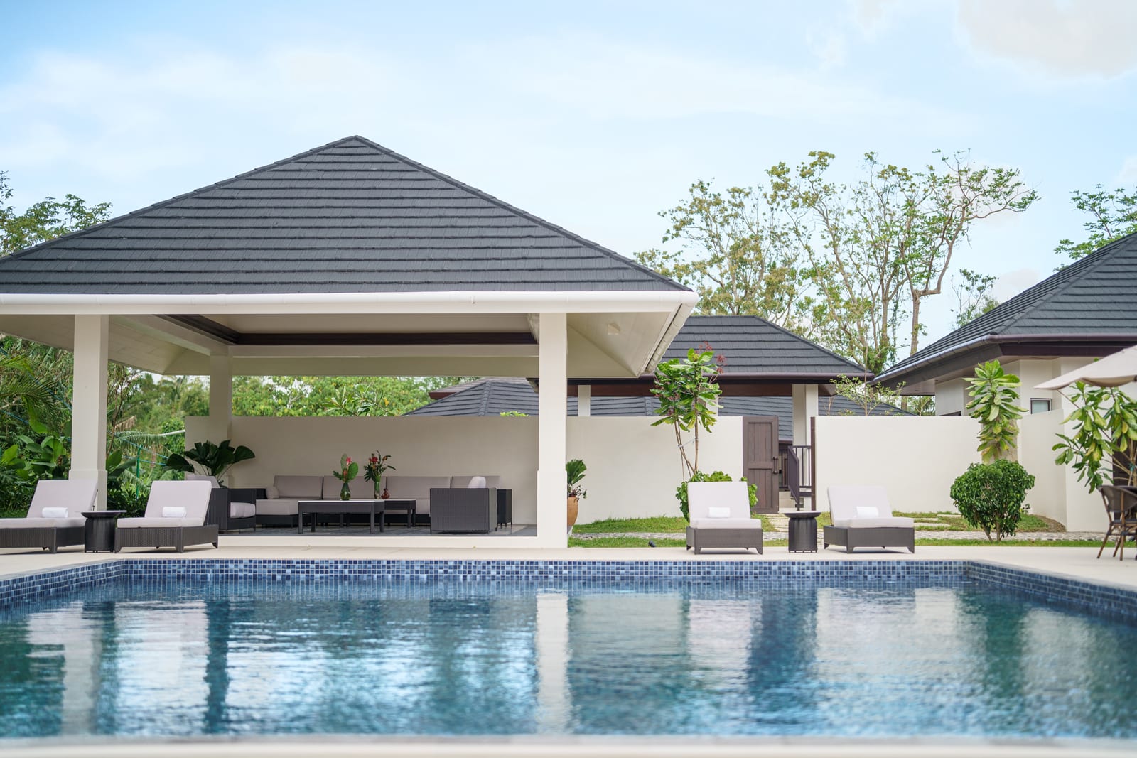 Luxury resort pavilion with dark pyramid roof overlooking tiled swimming pool and lounge seating area