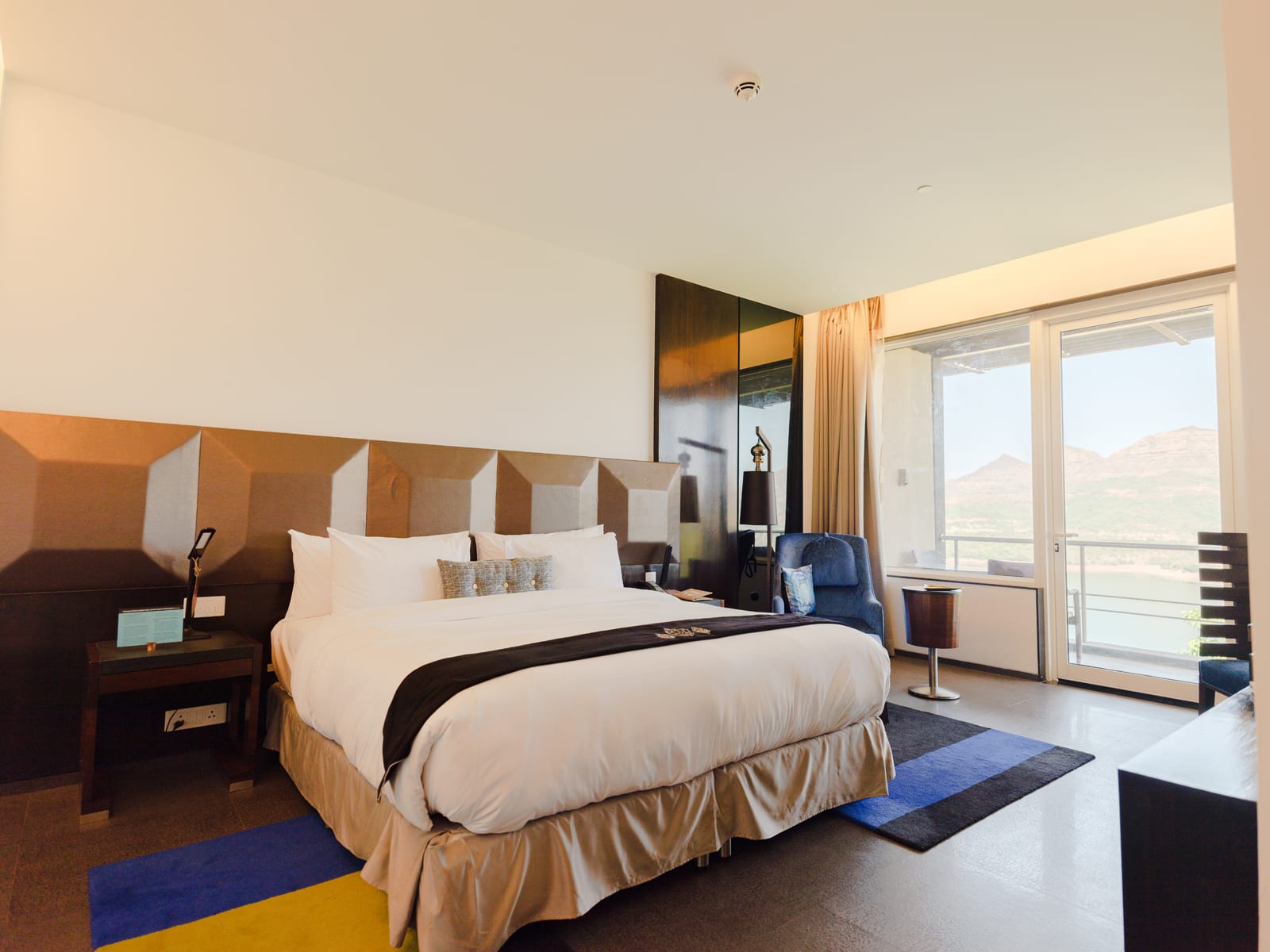 Modern hotel bedroom with geometric headboard, white bedding, and floor-to-ceiling windows overlooking mountains