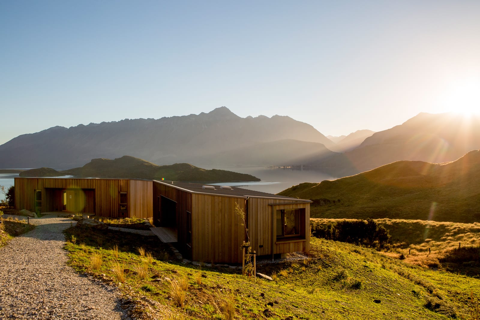 Modern corrugated metal cabin overlooking mountain lake at sunset in remote landscape