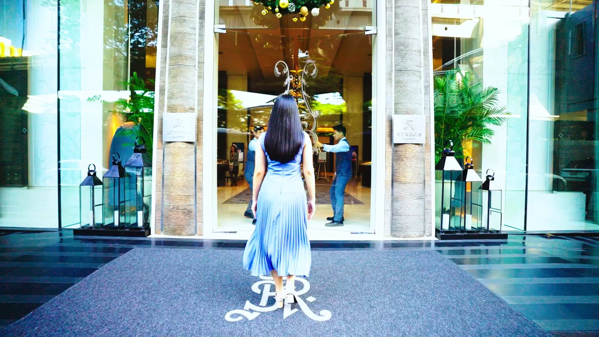 Woman in light blue pleated dress entering luxury boutique storefront with ornate door handle