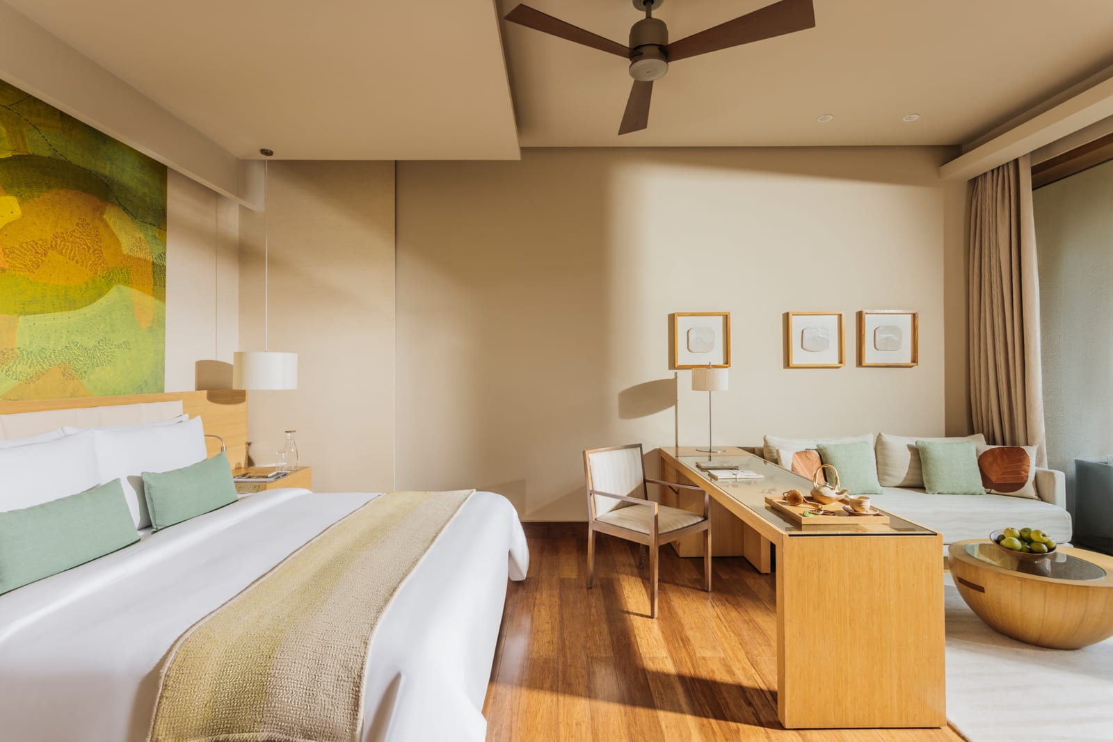 Modern hotel suite with queen bed, wooden desk, seating area, and nature-inspired artwork on walls