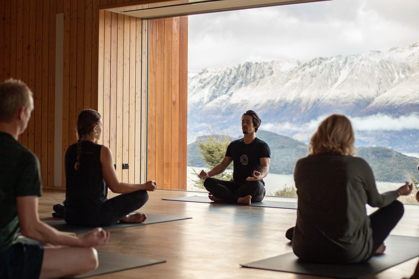Yoga instructor leading class in wooden studio with mountain and lake views through large windows