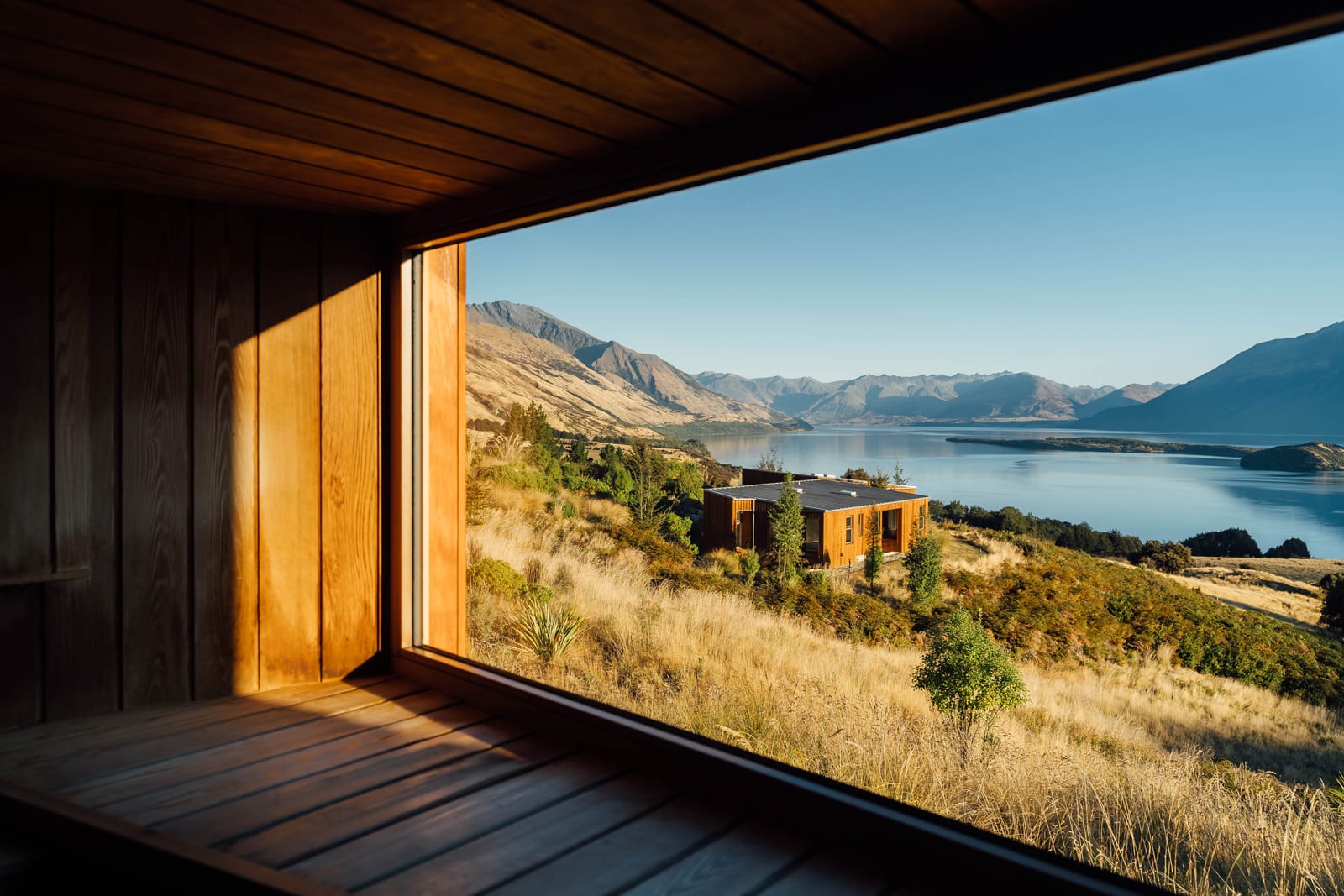 Modern wooden cabin interior with open door framing mountain lake and valley landscape