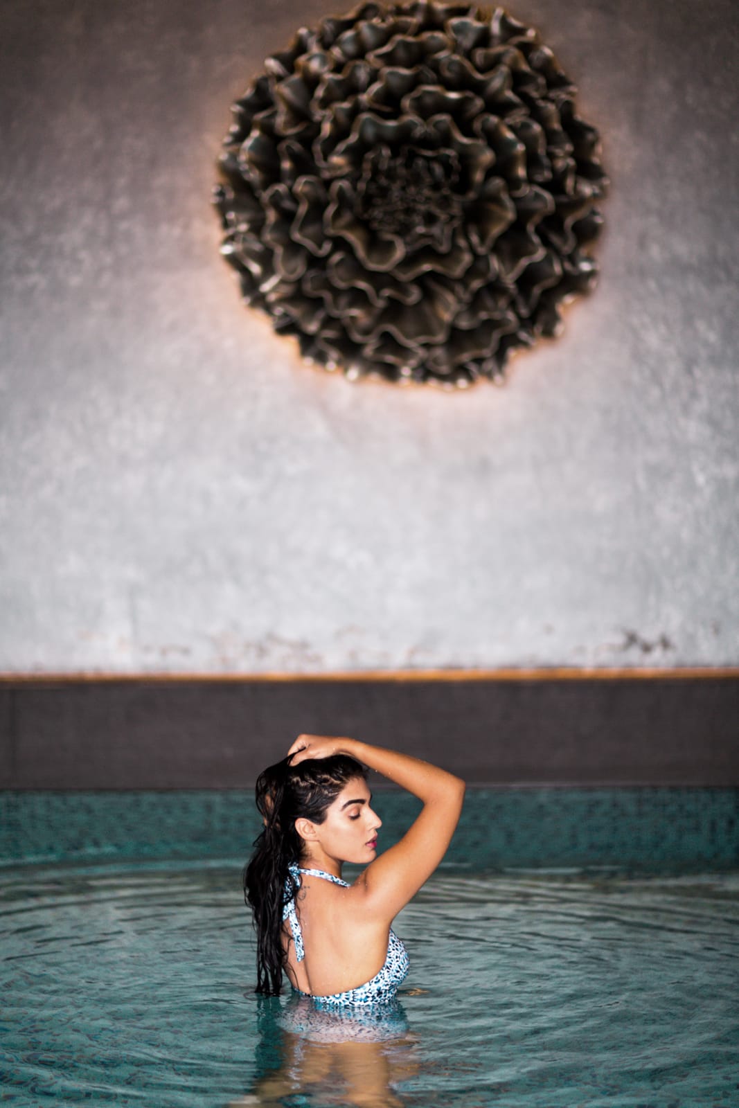 Woman in patterned bikini wading in turquoise water below textured brain coral formation