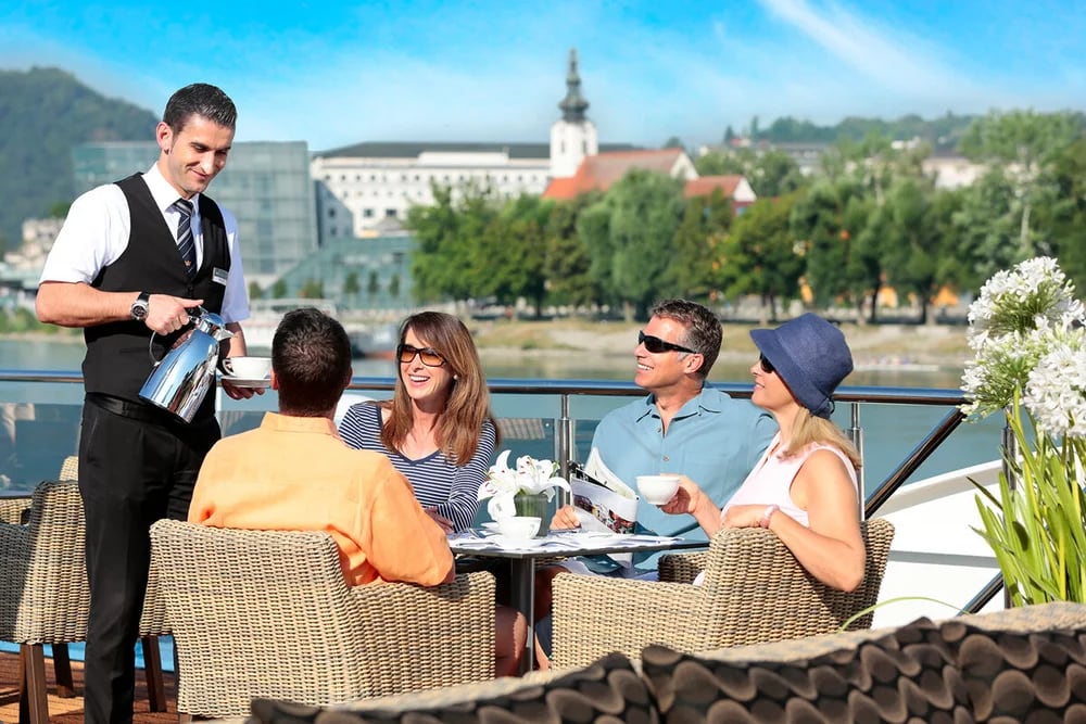 Waiter serving drinks to guests dining on riverside terrace overlooking church and cityscape