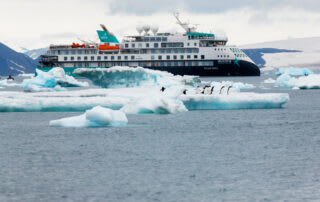 An Aurora Expeditions cruise ship navigating through icy waters with blue-white icebergs and