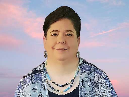 Woman with short dark hair wearing blue patterned cardigan and beaded necklace against sunset sky