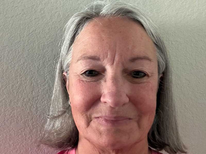 Middle-aged woman with gray hair and slight smile against neutral background