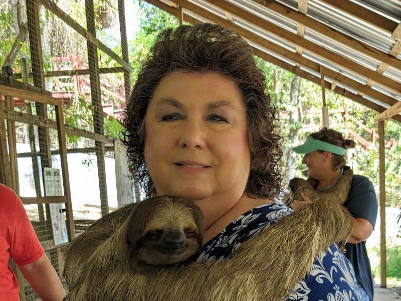 Woman holding a three-toed sloth in an outdoor enclosure