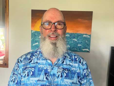 Bald man with long gray beard wearing blue Hawaiian shirt and glasses, smiling at camera
