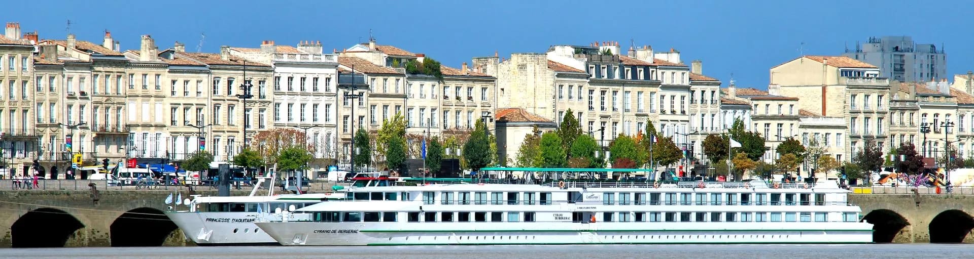 A modern river cruise ship moored along the Garonne River in Bordeaux, France, with classic 19th-century Haussmann-style buildings lining the waterfront.