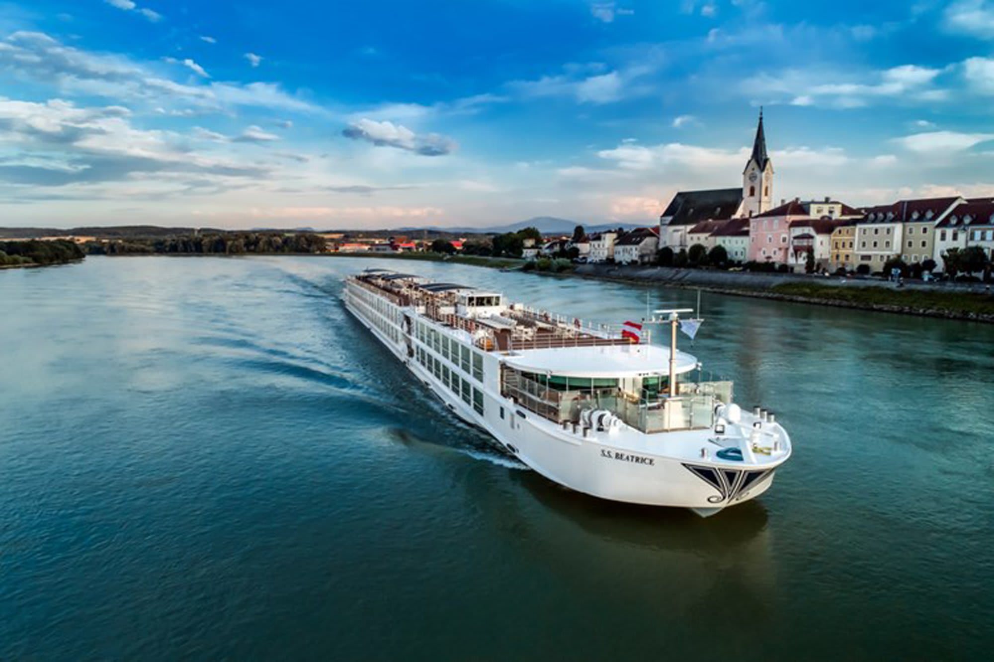 River cruise ship sailing past a charming European riverside town with church spire and colorful architecture on the Danube