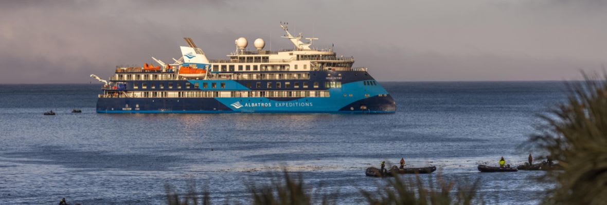The Polar Latitudes expedition cruise ship anchored in calm coastal waters with small Zodiac boats nearby.