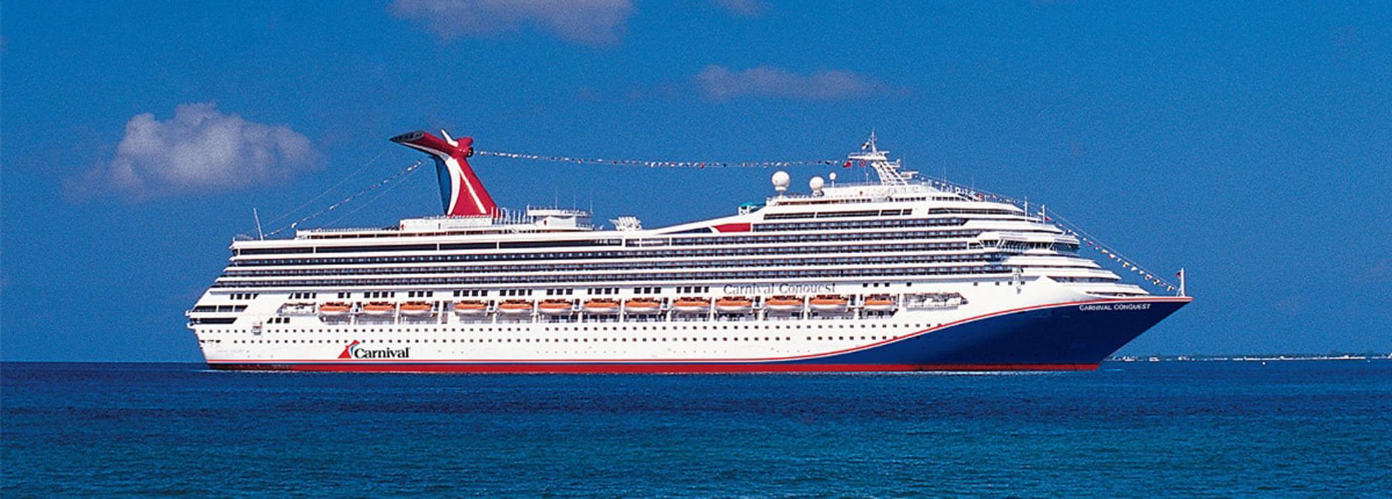 Carnival Cruise Ship at Sea A large white and red Carnival cruise ship sailing on deep blue ocean waters under a clear blue sky with soft clouds.