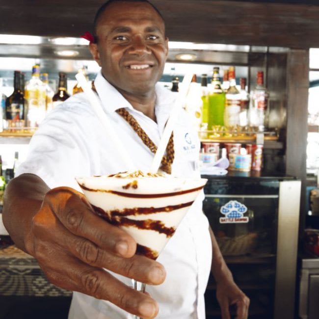 A smiling chef in white chef's coat presents an elegantly plated dessert with chocolate drizzle