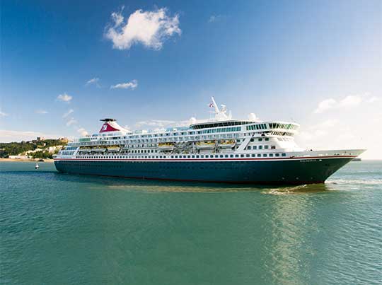 A large modern cruise ship is anchored in crystal-clear turquoise waters near a tropical beach