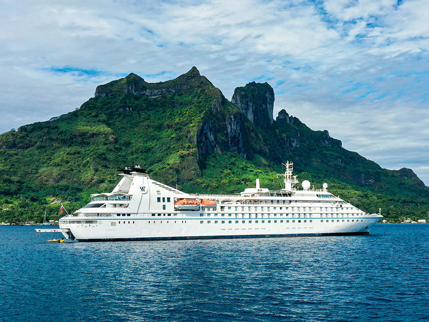 A pristine white cruise ship anchored in turquoise waters near a lush green mountainous island